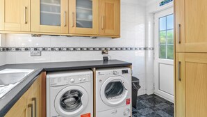 A laundry area with two washing machines, wooden cabinets, and a tiled backsplash.