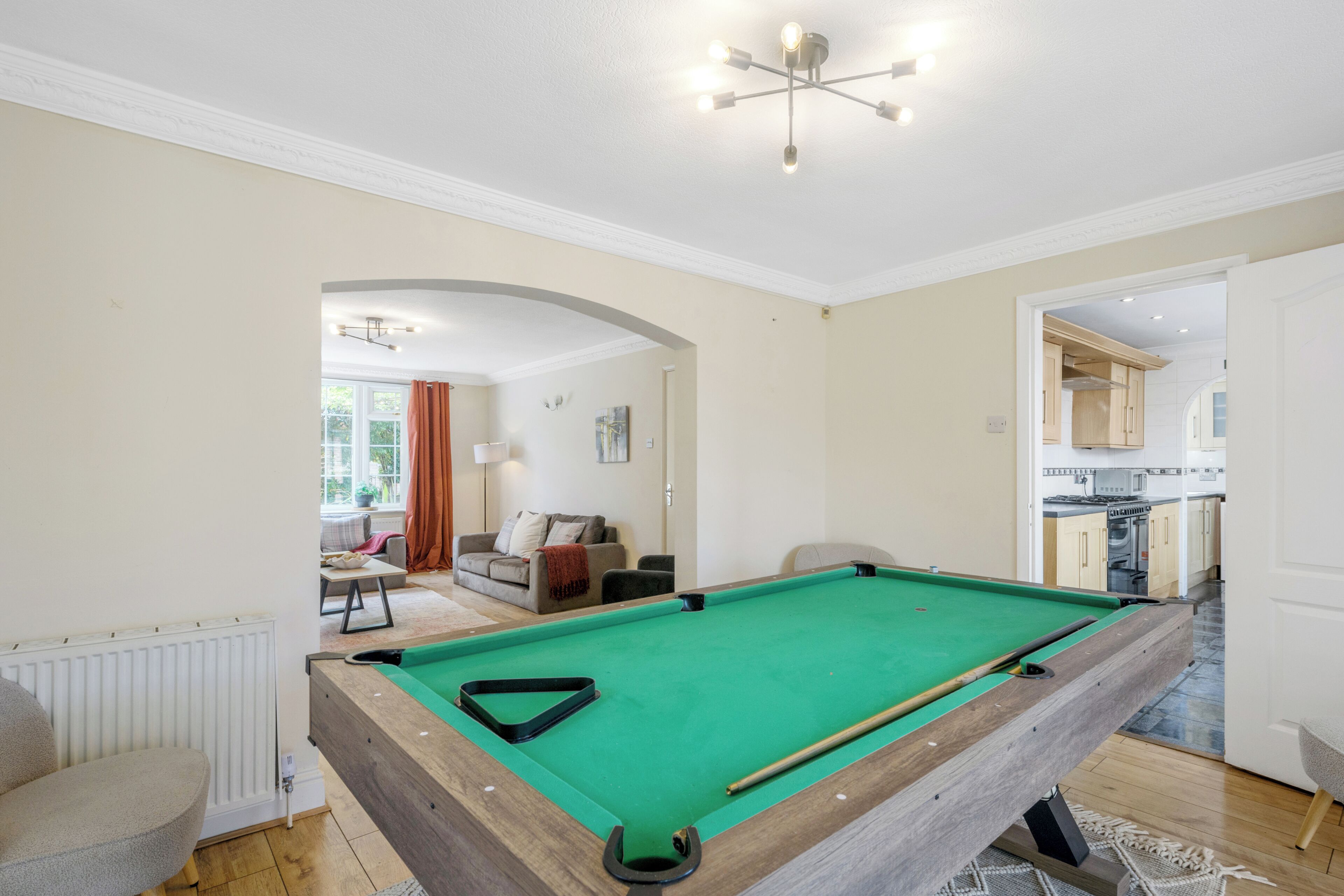 A pool table in a room with a view to a living area and kitchen.