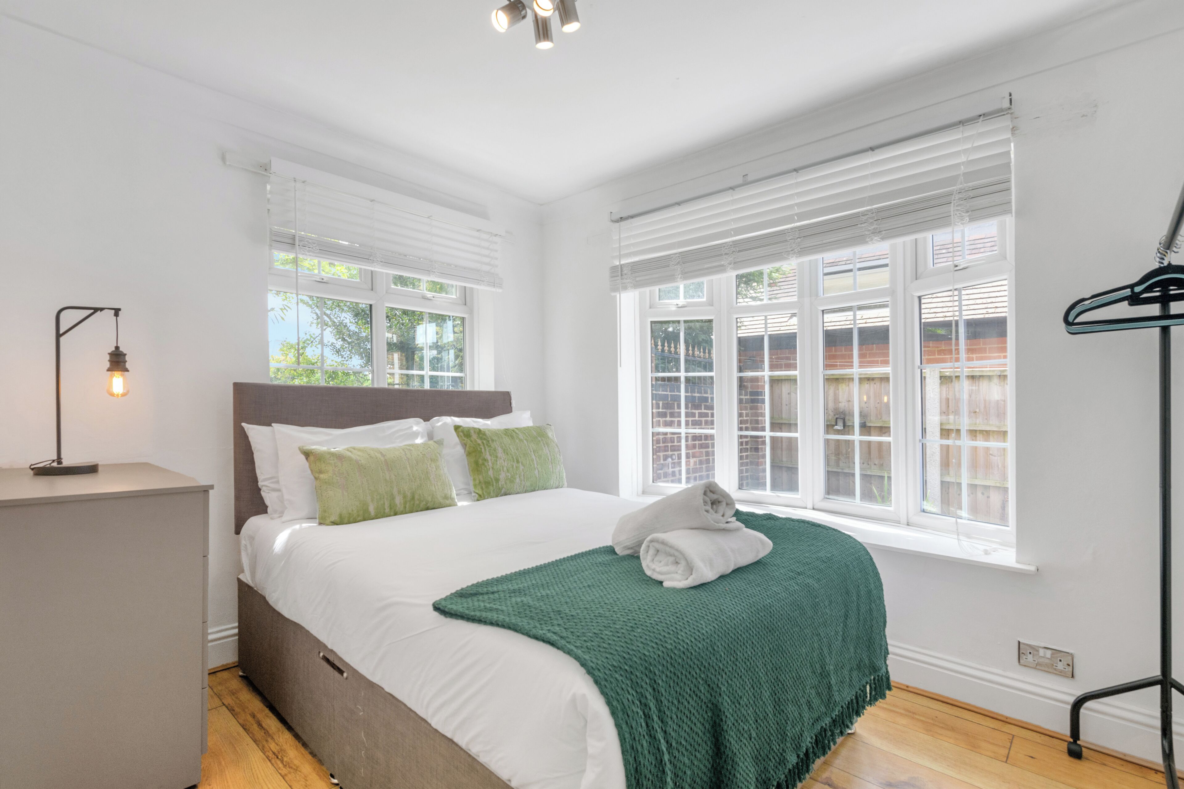 A bedroom with a bed, a bedside table, a lamp, and a window with blinds.