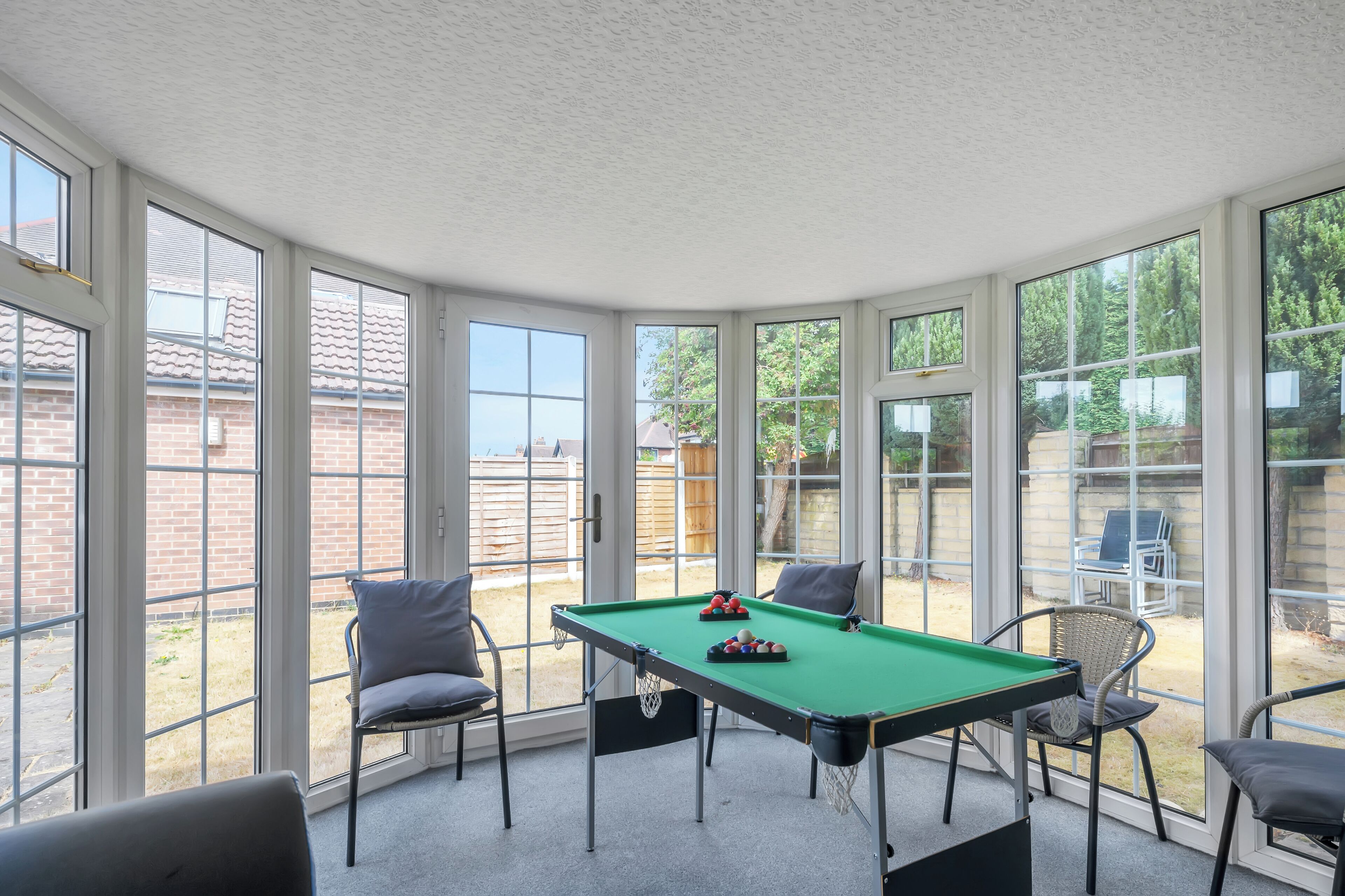 A pool table in a room with large windows, chairs, and a view of a backyard.
