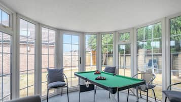 A pool table in a room with large windows, chairs, and a view of a backyard.
