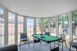 A pool table in a room with large windows, chairs, and a view of a backyard.