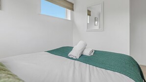 A bedroom with a bed, a window with a blind, a wall-mounted mirror, and a green textured throw blanket.
