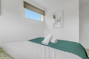 A bedroom with a bed, a window with a blind, a wall-mounted mirror, and a green textured throw blanket.