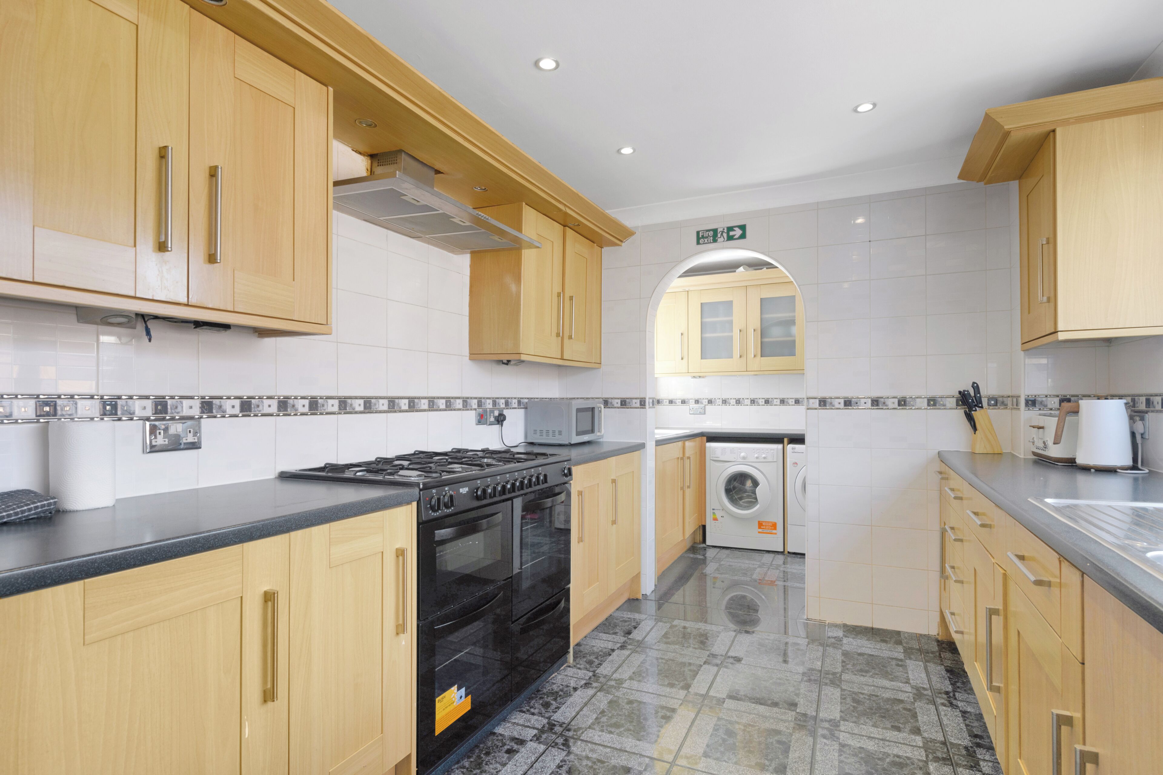A modern kitchen with wooden cabinets, a black stove, a microwave, and a washing machine.