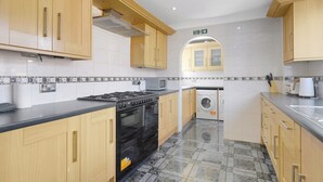 A modern kitchen with wooden cabinets, a black stove, a microwave, and a washing machine.