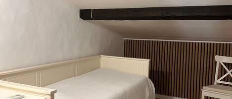A small, single-bed room with a sloped ceiling, a wooden chair, and a patterned rug.