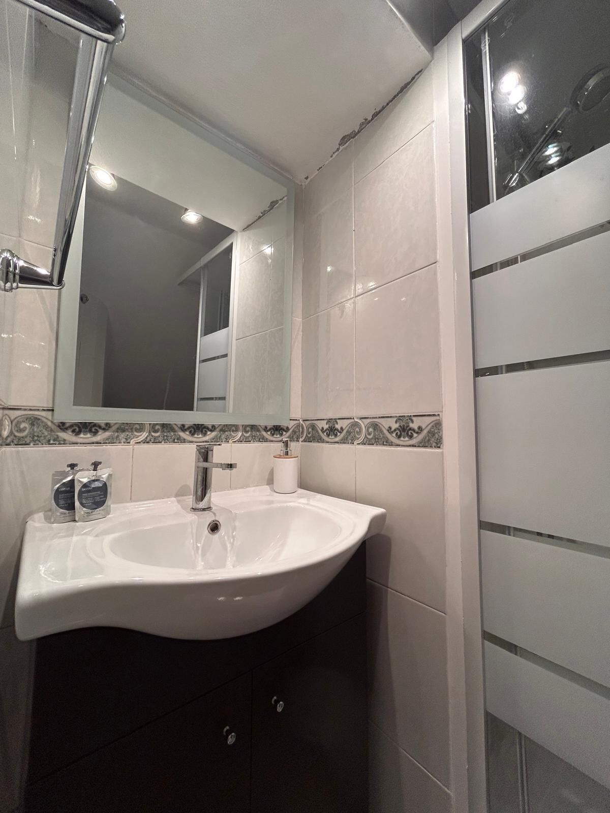 Un baño moderno con un lavamanos blanco, un espejo y una zona de ducha.