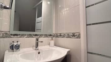 Un baño moderno con un lavamanos blanco, un espejo y una zona de ducha.