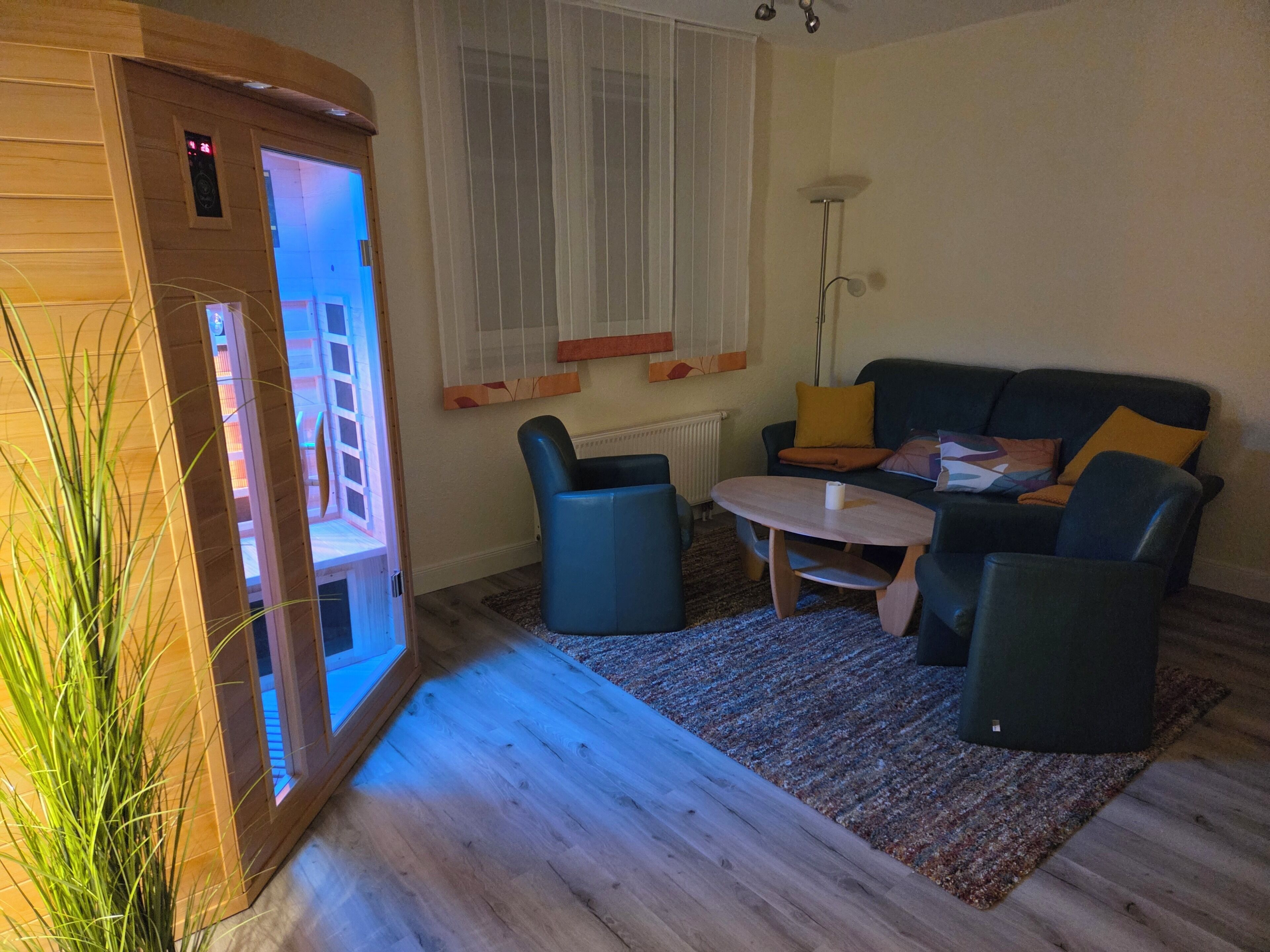 Ein Wohnzimmer mit Massagesessel, Sofa, Couchtisch und Heizkörper.