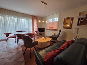 Ein modernes Wohnzimmer mit einem grünen Sofa, roten Sesseln, einem runden Couchtisch und einem Fernseher.