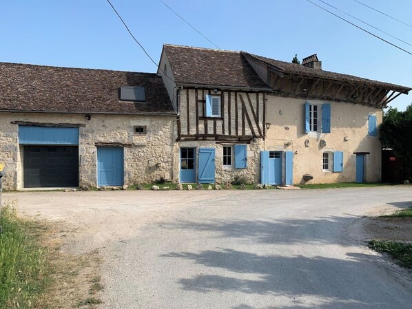 A two-story stone building with a dirt driveway and blue shutters. - Vrbo Property (Plaisance)