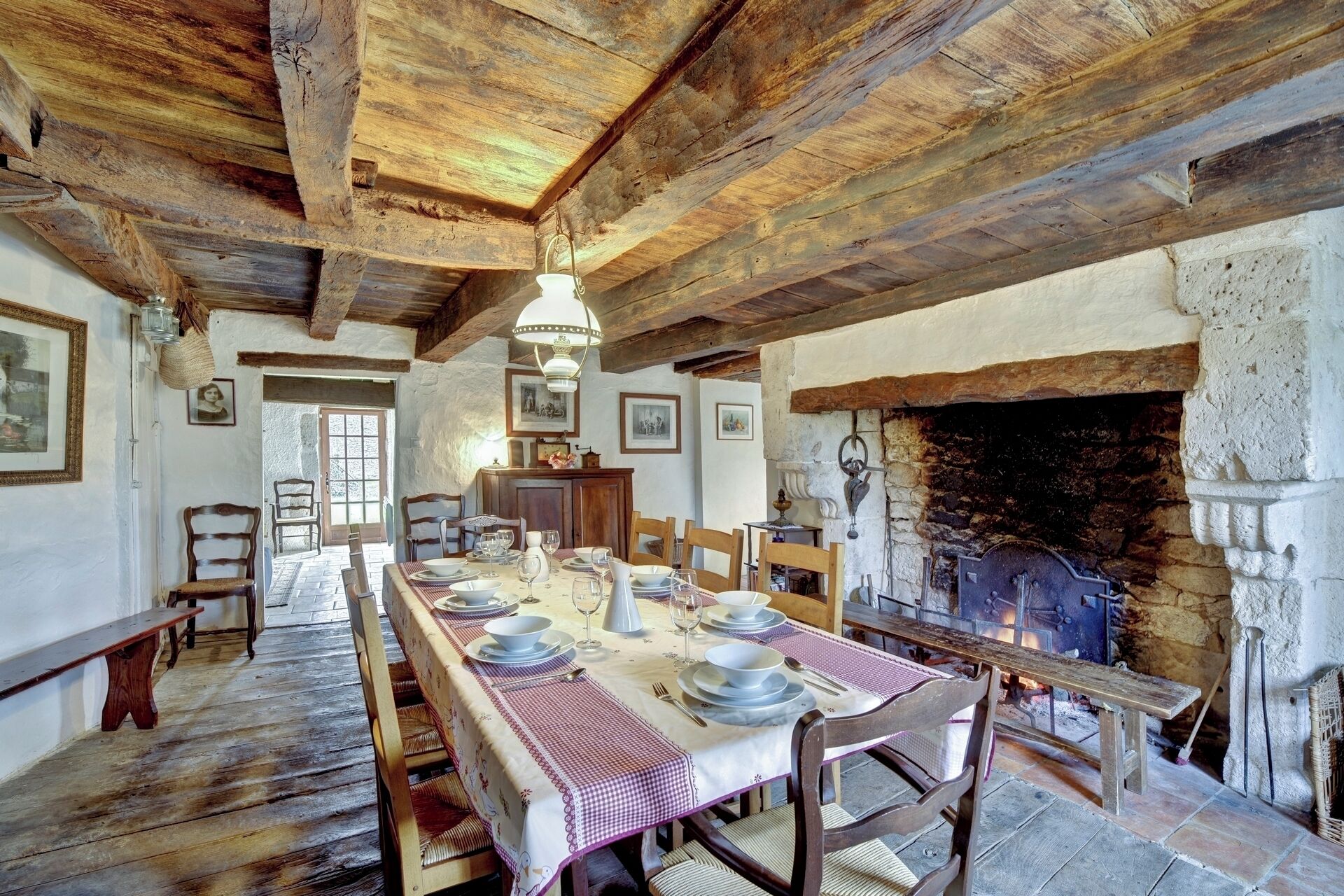 Een rustieke eetkamer met een lange tafel voor zes personen, houten balken in het plafond en een stenen open haard.