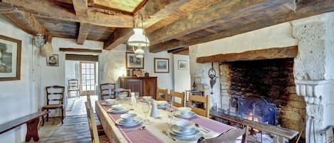Un comedor rústico con una larga mesa dispuesta para seis personas, vigas de madera en el techo y una chimenea de piedra.