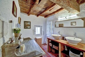 A rustic bathroom with wooden beams, a large mirror, two sinks, and a window. - Vrbo Property (Plaisance)