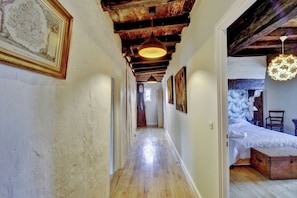 A narrow hallway with wooden floors and exposed beams, leading to a bedroom with a bed and a wooden chest. - Authentic, renovated 3-bedroom house in the Périgord region (Plaisance)