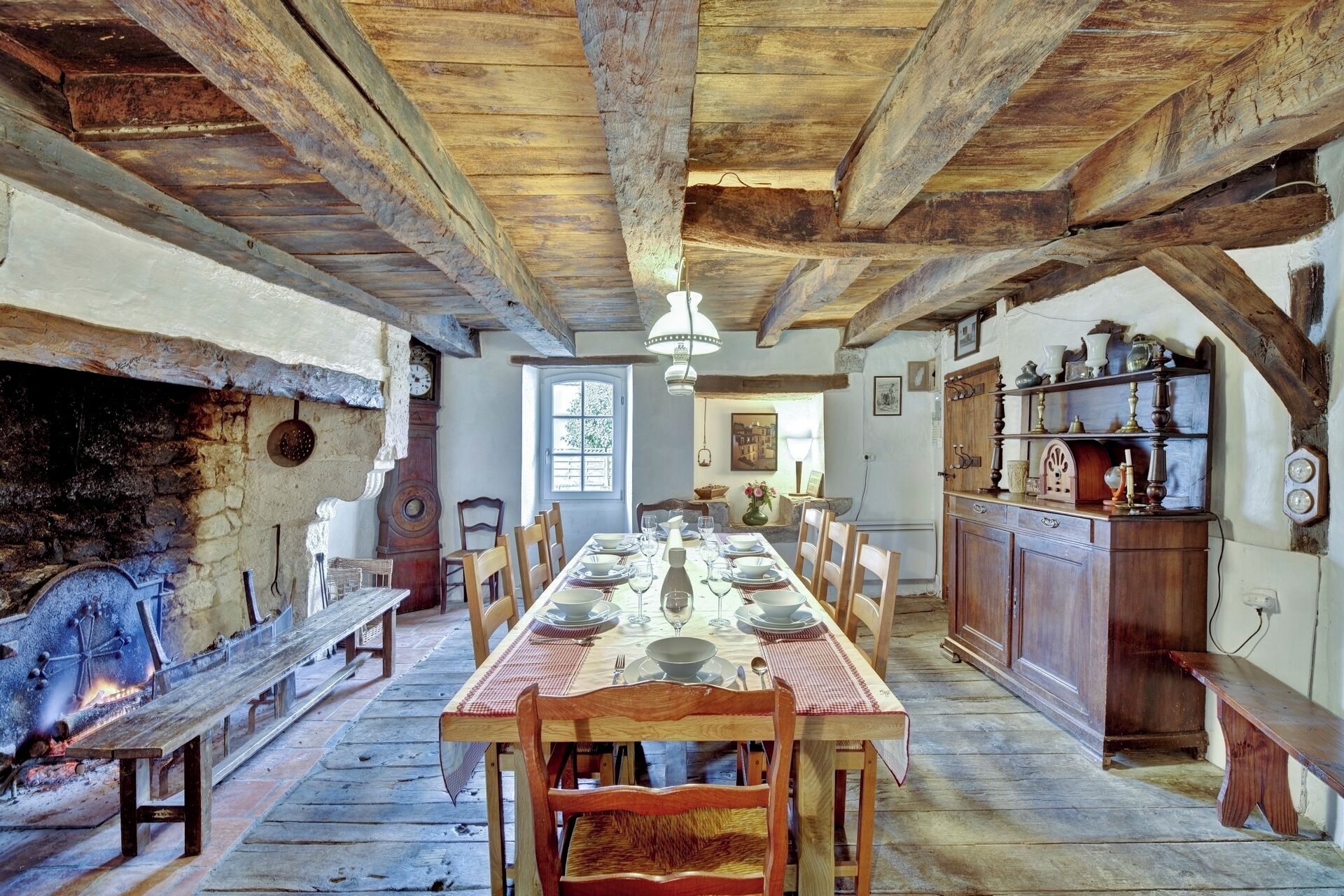 Un comedor rústico con una larga mesa de madera dispuesta para una comida, flanqueada por bancos de madera y una chimenea de piedra.