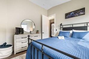 Une chambre à coucher avec un lit, une commode, un miroir, un téléviseur et un tableau accroché au mur.