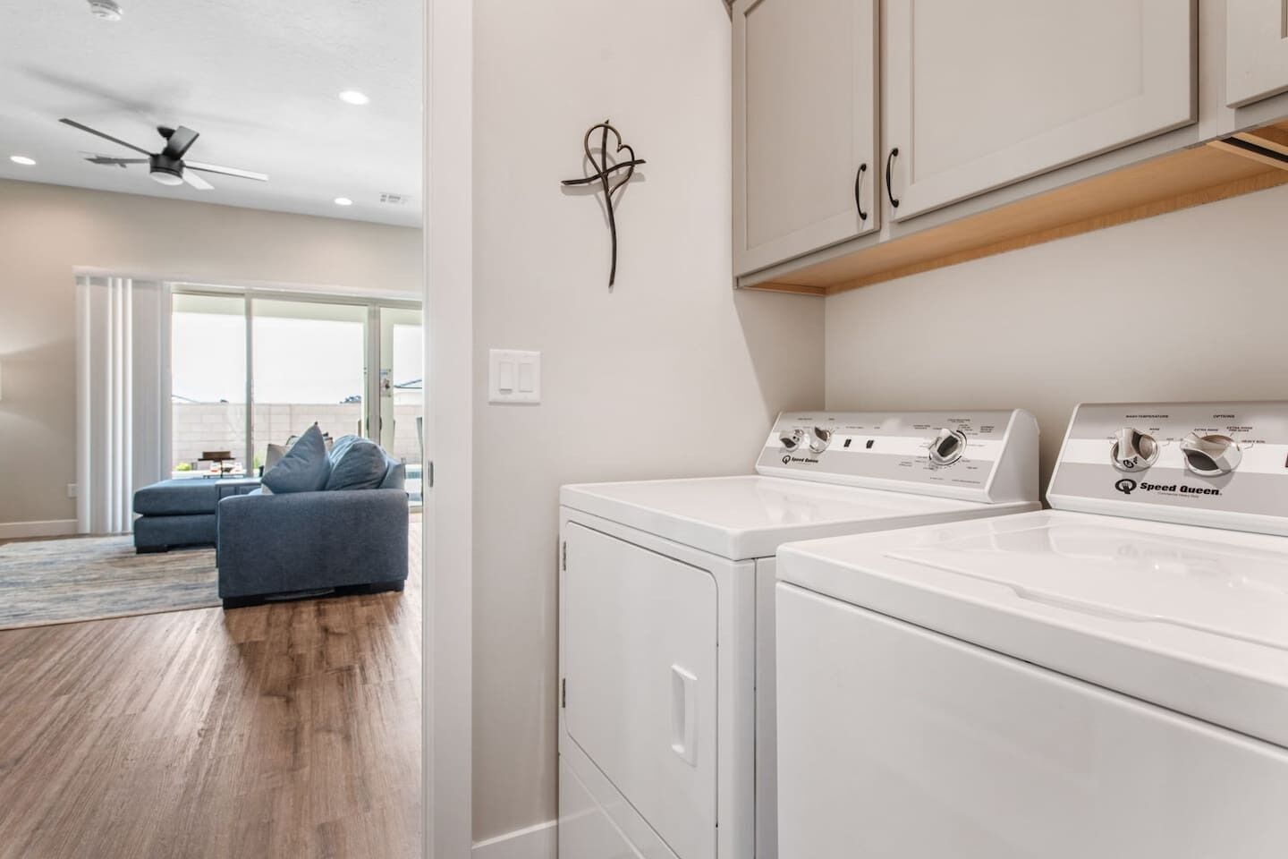 A laundry room with two white washing machines, a ceiling fan, and a wall-mounted cabinet.