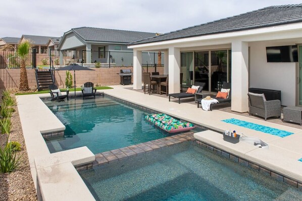 A swimming pool with lounge chairs and a hot tub area.