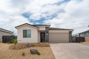 A modern single-story house with a garage, a driveway, and a landscaped front yard with rocks and plants.