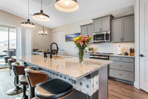 A modern kitchen with a central island, bar stools, a microwave, and a dining area with a view. - Grill and Chill by J and Amy BL 992912 (Mesquite)
