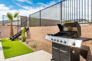 Un espace extérieur aménagé pour les barbecues, avec un gril en acier inoxydable, un petit escalier et un palmier.