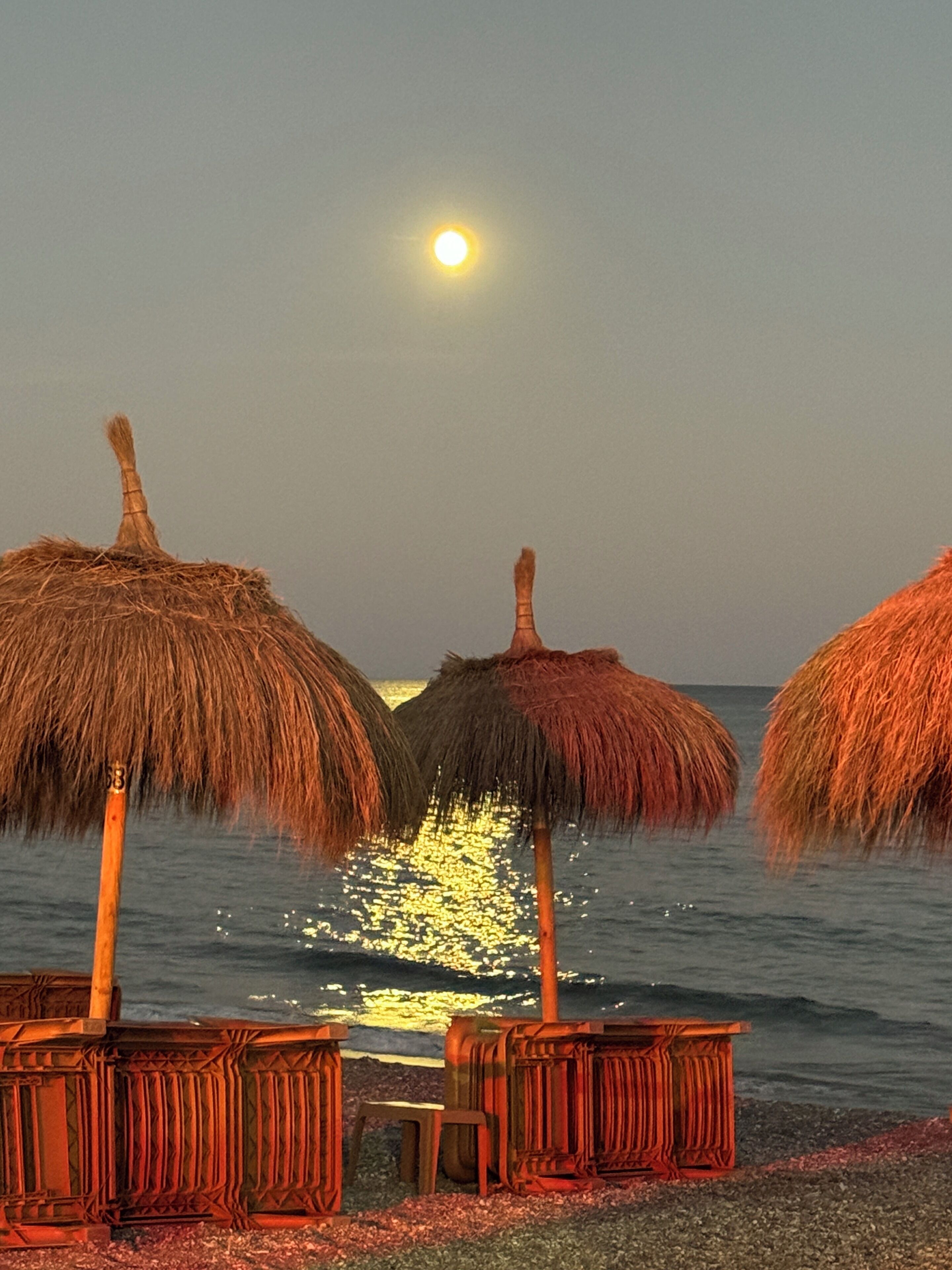 Une scène de plage avec des parasols en chaume et des meubles en bois, le tout installé au bord de l’eau.