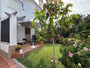 Ein Wohnhaus mit überdachter Terrasse, Sitzgelegenheiten im Freien und einem gepflegten Garten.
