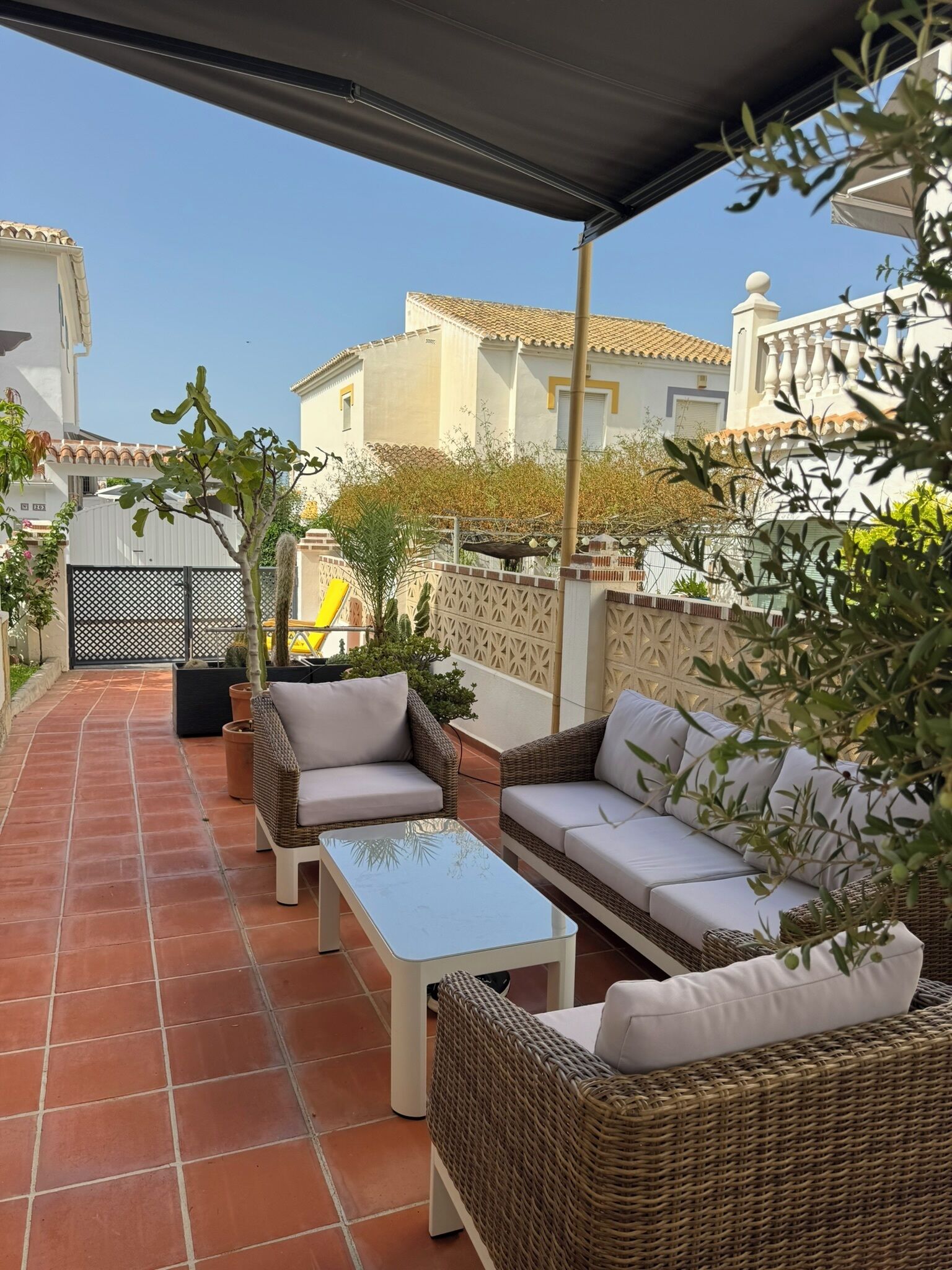 Un patio con mobiliario exterior, piso de baldosas y vista de edificios al fondo.