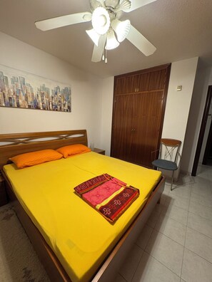 Ein Hotelzimmer mit einem Bett, einem Holzschrank, einem Sessel und einem Deckenventilator.