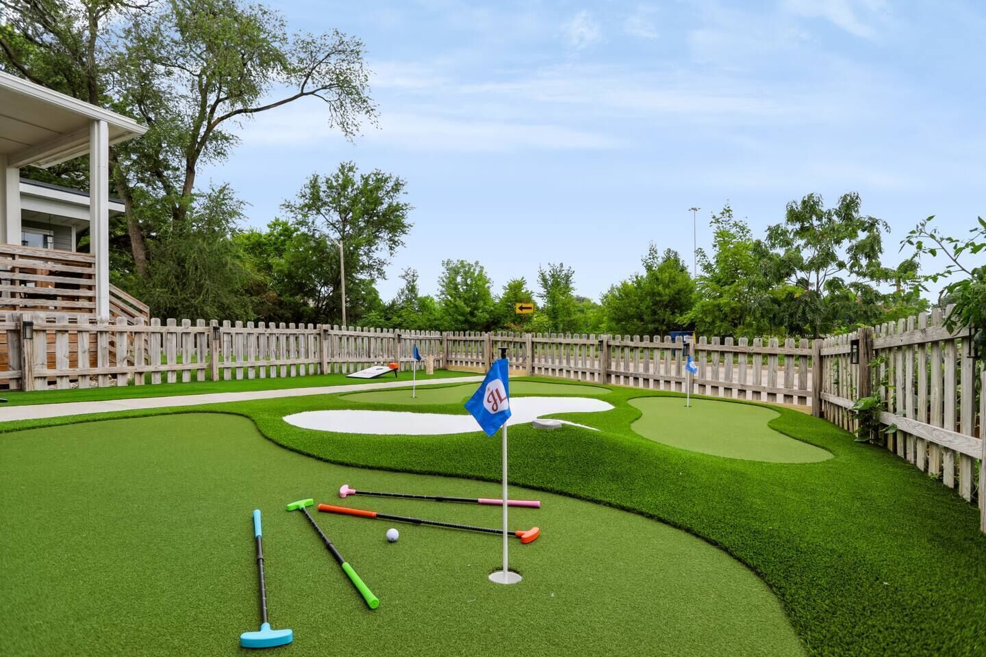 A miniature golf course with a wooden fence, a flag, and golf clubs.