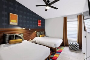 Ein Hotelzimmer mit zwei Betten, einem Deckenventilator, einem Fenster mit Vorhängen und einem farbenfrohen Teppich.