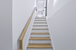 Eine moderne Treppe mit Holzsitzstufen und einem Metallgeländer, die zu einem hellen Flur führt.