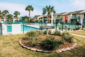 Une zone abritant une piscine, avec un panneau indiquant « DAMON POINT », entourée de palmiers et d’une clôture.