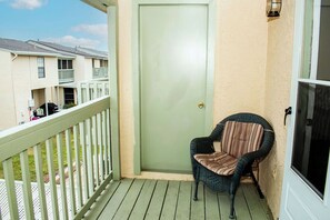 Un balcon avec une porte, une chaise en osier et une vue sur les immeubles voisins.