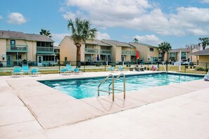 A swimming pool with lounge chairs and a palm tree, surrounded by multi-story buildings with balconies. - Cozy 2-bedroom condo with AC in welcoming Panama City Beach (Panama City Beach)