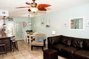 A living room with a brown leather sofa, a dining area with a table and chairs, and a kitchen with a bar. - Cozy 2-bedroom condo with AC in welcoming Panama City Beach (Panama City Beach)