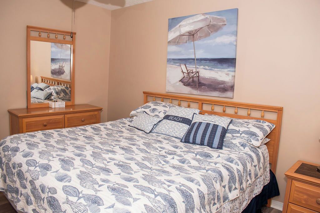 Una camera da letto con un letto, una cassettiera, un comodino, uno specchio e un quadro a tema spiaggia.