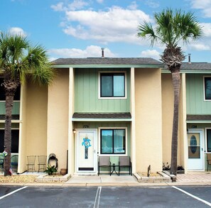 A two-story building with a green and beige facade, numbered 126 and 124, featuring a front door with a blue doorbell, two windows, and a small seating area with chairs. - Cozy 2-bedroom condo with AC in welcoming Panama City Beach (Panama City Beach)