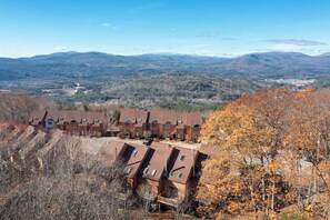 A residential area with multiple brick buildings, likely a dormitory or apartment complex, surrounded by autumn foliage and distant mountains. - Waterville Estates Condo- Hot Tub- Pools- Ski Mtn (Campton)
