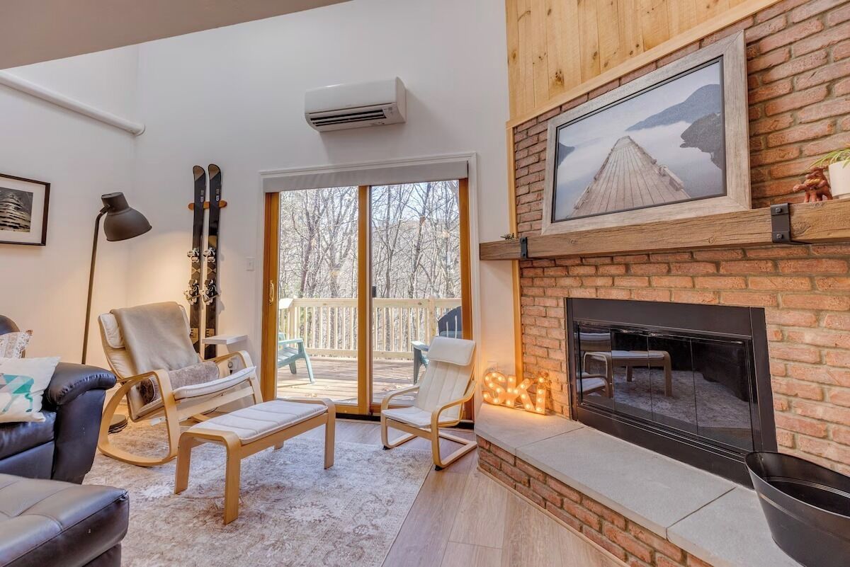 Ein Wohnzimmer mit Kamin, Skiständer und großem Fenster mit Blick auf eine Terrasse.