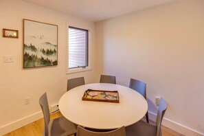 A dining area with a round table, four chairs, a window with blinds, and two framed pictures on the wall. - Waterville Estates Condo- Hot Tub- Pools- Ski Mtn (Campton)