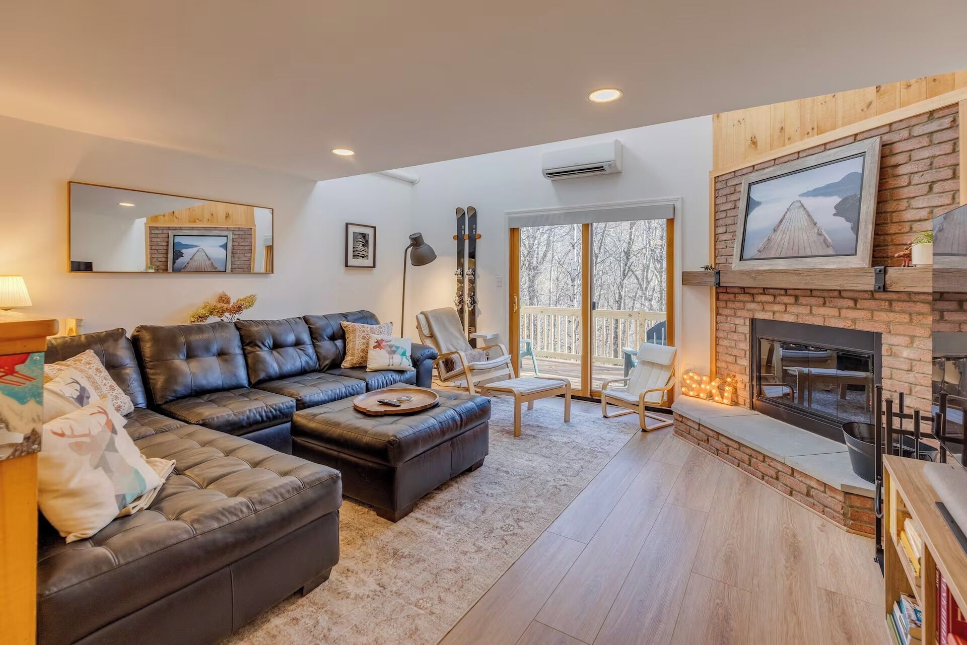 A living room with a fireplace, leather sofa, and a large window overlooking a snowy landscape.