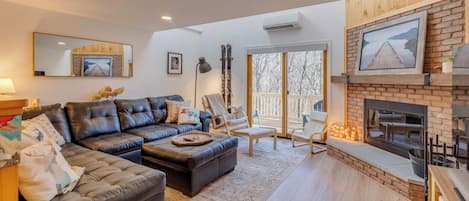A living room with a fireplace, leather sofa, and a large window overlooking a snowy landscape.