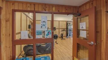 Een kamer met houten lambrisering en fitnessapparatuur, waaronder een hometrainer en een ventilator.