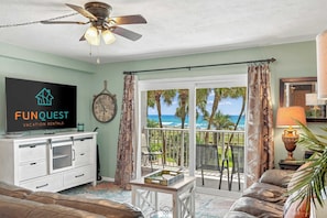 A living room with a TV, a clock, a ceiling fan, a view of the ocean, and a balcony with curtains. - The Summit 225 - Ocean Views & Beach Vibes (Panama City Beach)