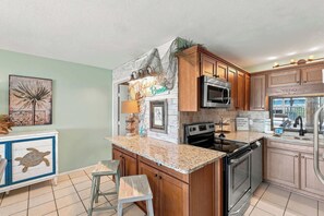 A kitchen with wooden cabinets, a granite countertop, a stainless steel oven, and a microwave. - The Summit 225 - Ocean Views & Beach Vibes (Panama City Beach)