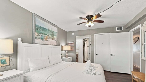 A bedroom with a bed, bedside tables, a ceiling fan, and a door leading to a bathroom. - The Summit 225 - Ocean Views & Beach Vibes (Panama City Beach)