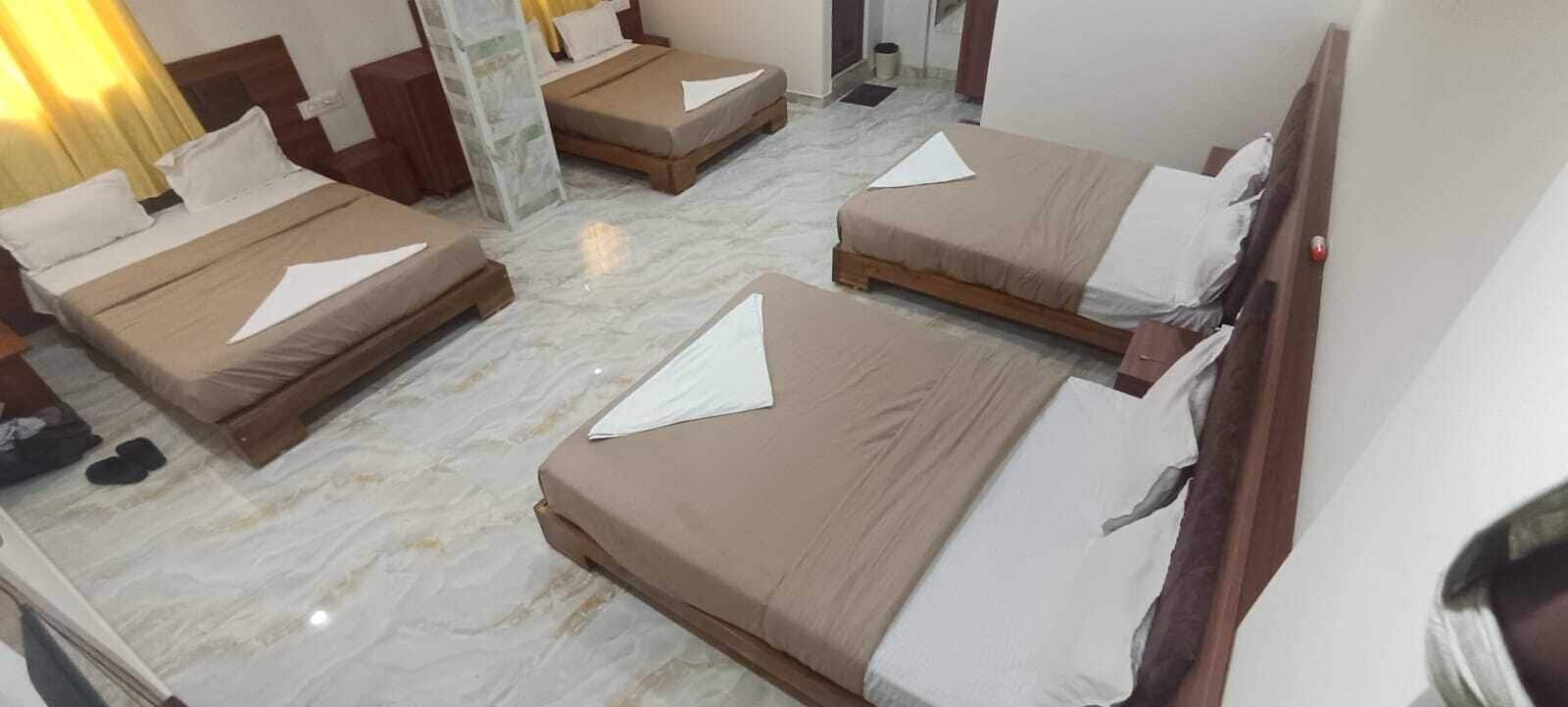 A hotel room with four beds arranged in a square layout, a marble floor, and a wooden headboard.